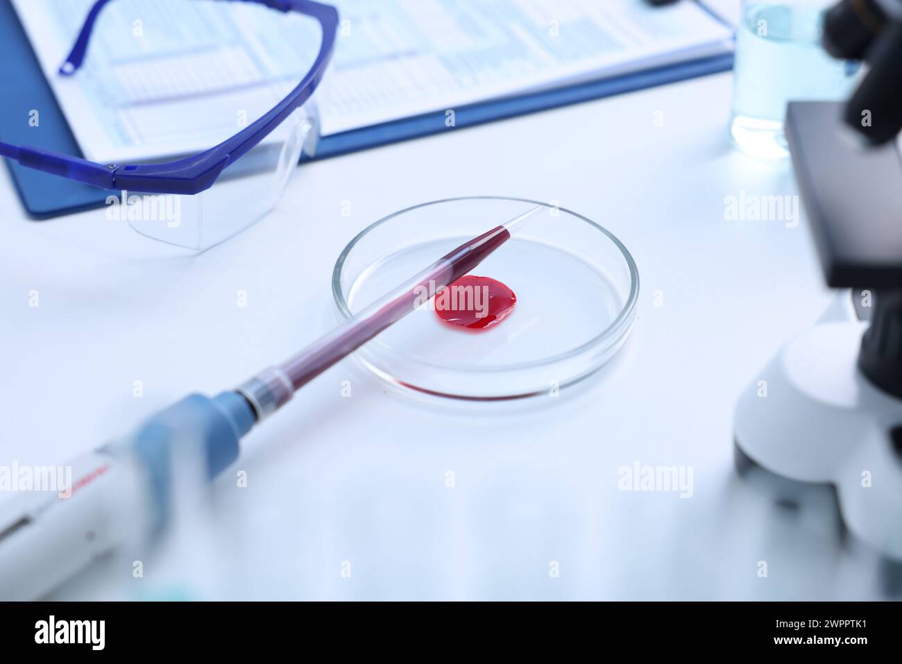 Gocciolamento del campione di sangue sulla piastra Petri su un tavolo bianco in laboratorio, primo piano Foto Stock
