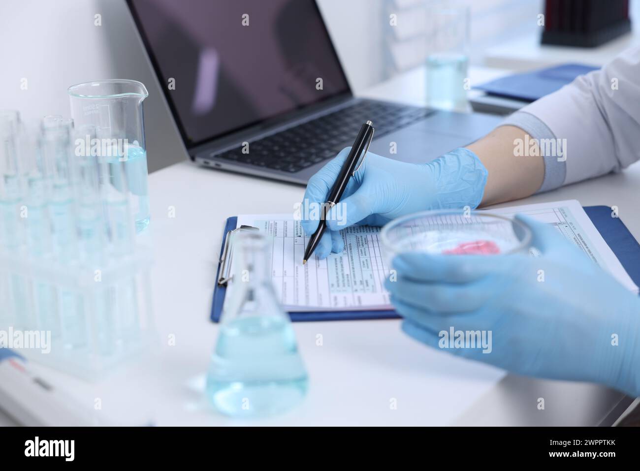 Operaio di laboratorio che tiene in mano una piastra di Petri con un campione di sangue mentre lavora al tavolo bianco, primo piano Foto Stock