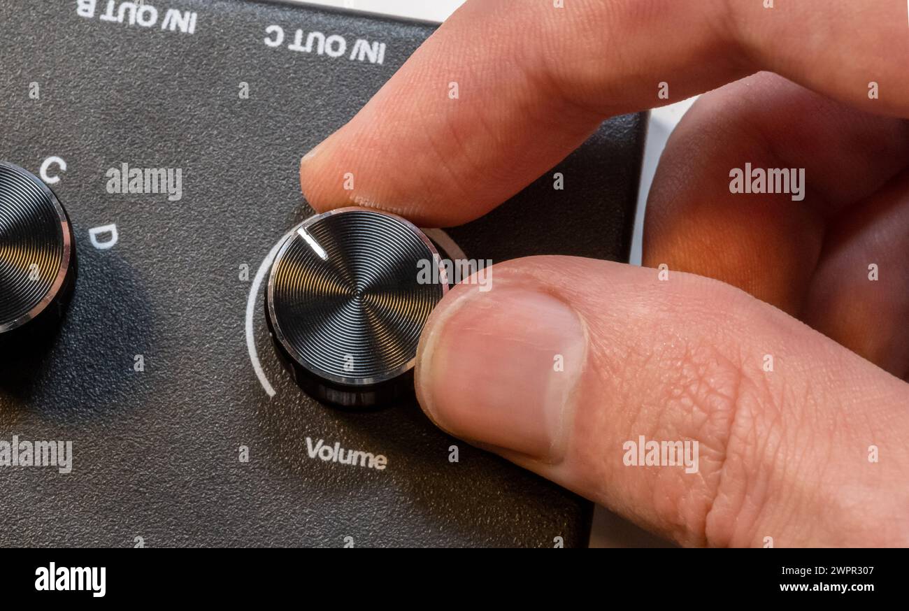 Un uomo anonimo può regolare con precisione una manopola del volume su un elegante pannello di controllo del dispositivo audio, regolare i livelli audio, controllare, alzare la musica, o. Foto Stock