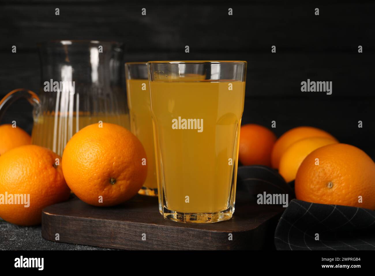 Molte arance mature e succo fresco su un tavolo grigio scuro Foto Stock
