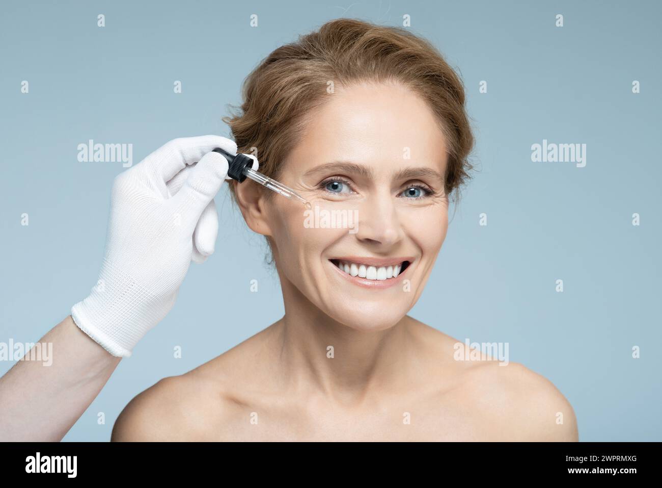 L'estetista tiene il contagocce per pipette con olio essenziale o siero vicino al viso di una donna adulta per idratare e idratare la pelle Foto Stock