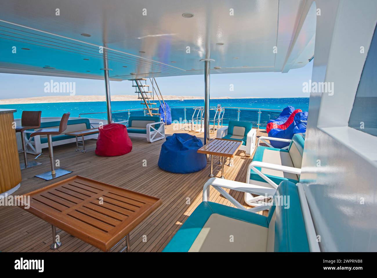 Terrazza solarium in legno di poppa di teak di un grande yacht a motore di lusso con sedie, divano tavolo e sfondo con vista sul mare tropicale Foto Stock