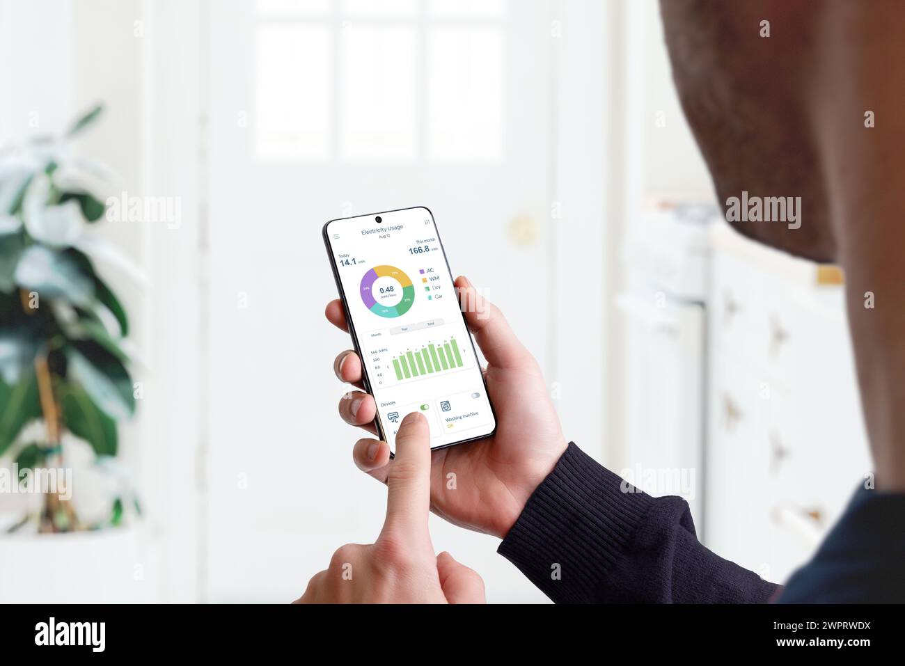 Guy monitora l'utilizzo dell'elettricità domestica con l'app Smart Home. Concetto di efficienza energetica, tecnologia e gestione domestica per una vita sostenibile Foto Stock
