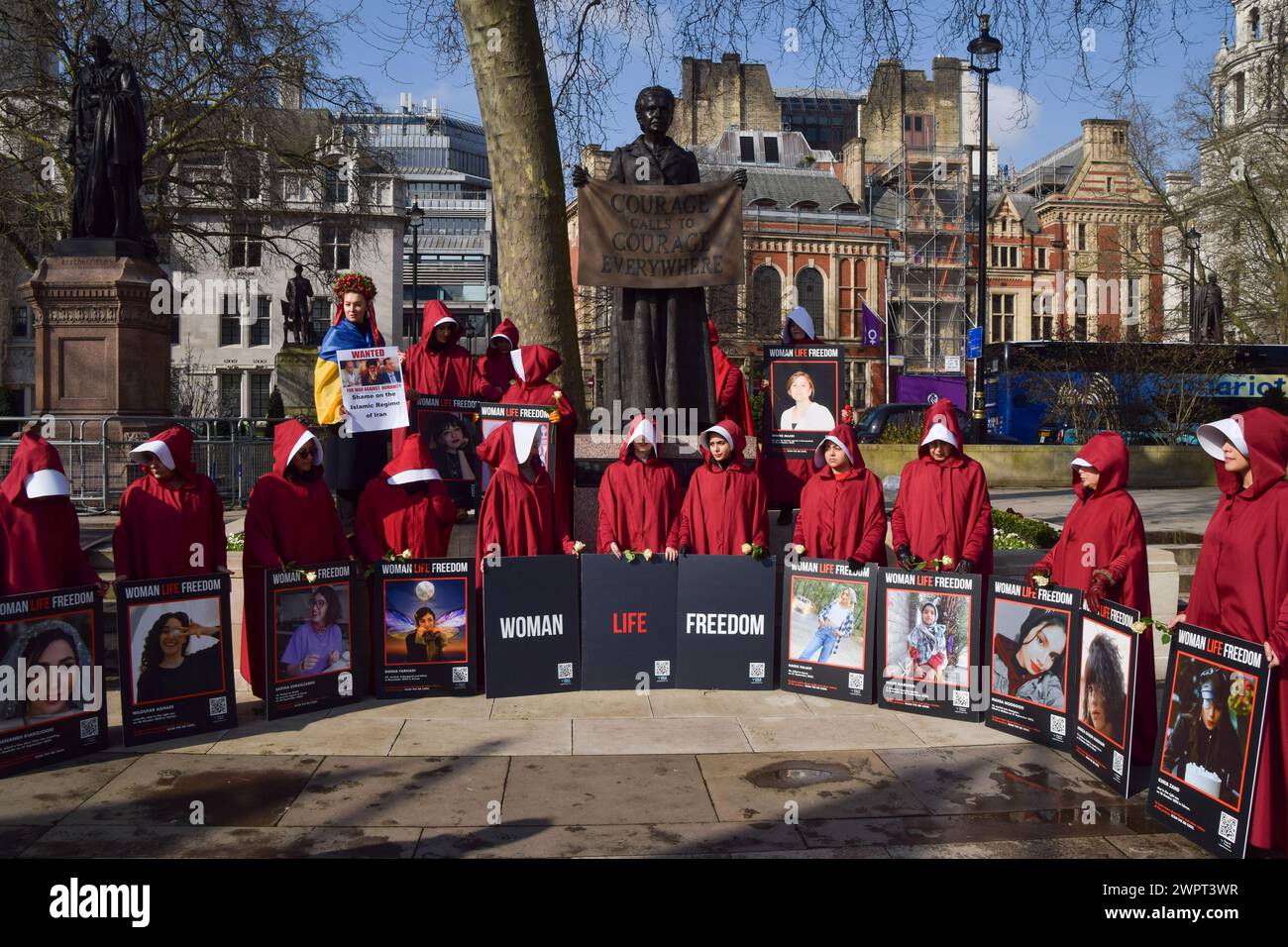 Londra, Regno Unito. 8 marzo 2024. I manifestanti si trovano accanto alla statua di Millicent Fawcett nella piazza del Parlamento con le immagini delle vittime del regime iraniano. Le donne che indossavano i costumi della Handmaid's tale hanno marciato attraverso il centro di Londra a sostegno della libertà per l'Iran in occasione della giornata internazionale della donna. Crediti: Vuk Valcic/Alamy Live News Foto Stock