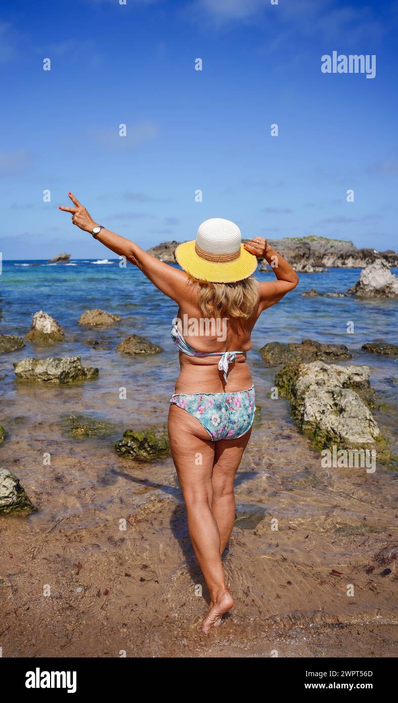 vista posteriore di una donna matura con cellulite che guarda all'orizzonte sulla spiaggia. Positività corporea e concetto di accettazione Foto Stock