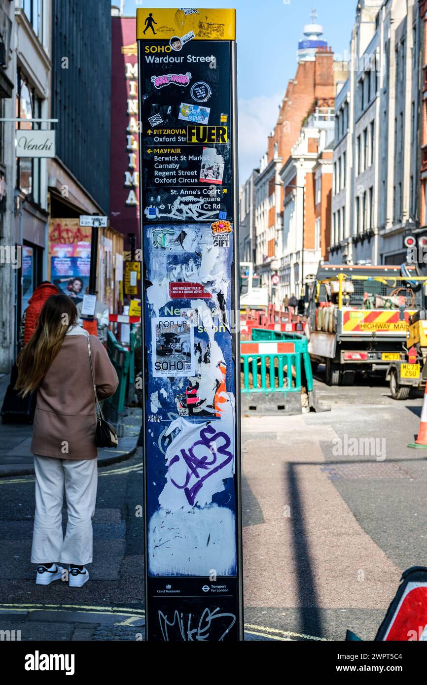 Soho, Londra Regno Unito, 08 marzo 2024, Anonymous Woman Back to camera Standing Next to Graffiti vandalizzato Direction Street Map Foto Stock