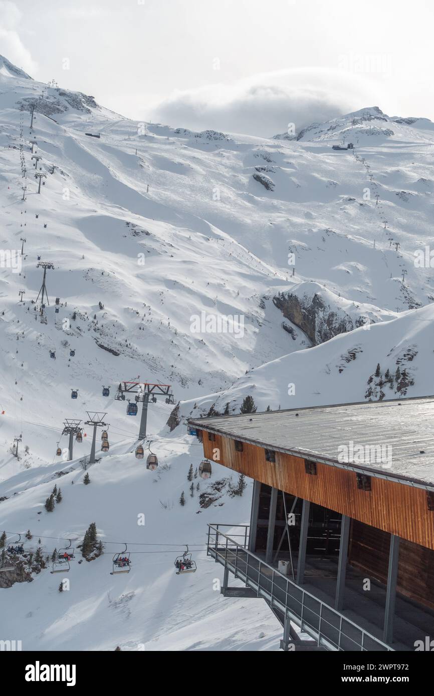 Cabine da sci parcheggiate, gondole in una grande casa di legno, preparatevi per la guida, e una pista da sci in lontananza, Hintertux, Autria Foto Stock