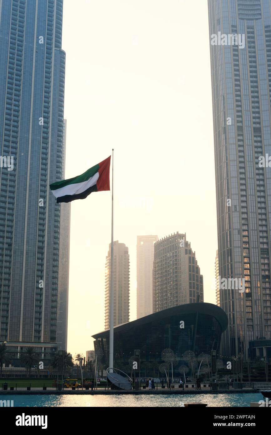 La bandiera degli Emirati Arabi Uniti si apre al tramonto tra i grattacieli di Dubai. Dubai, Emirati Arabi Uniti - 15 agosto 2023 Foto Stock