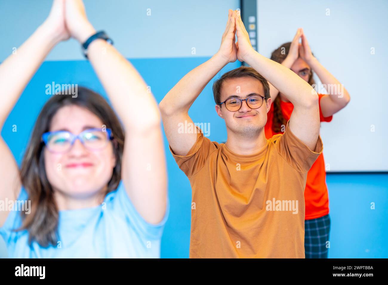 Gruppo felice di disabili che alzano le braccia praticando yoga in palestra Foto Stock
