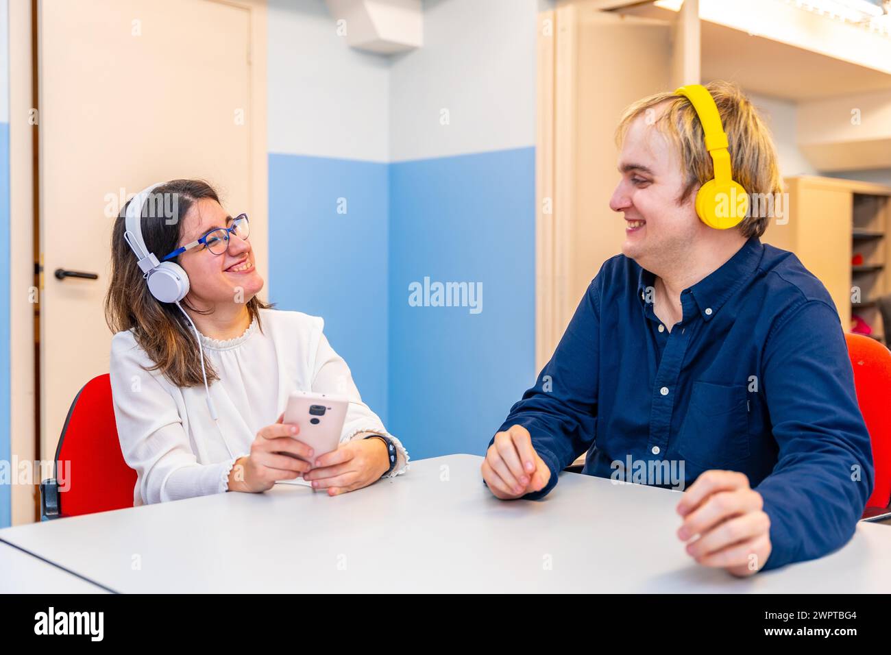 Amici con disabilità mentali che condividono musica utilizzando il telefono e le cuffie in un centro di assistenza diurna Foto Stock