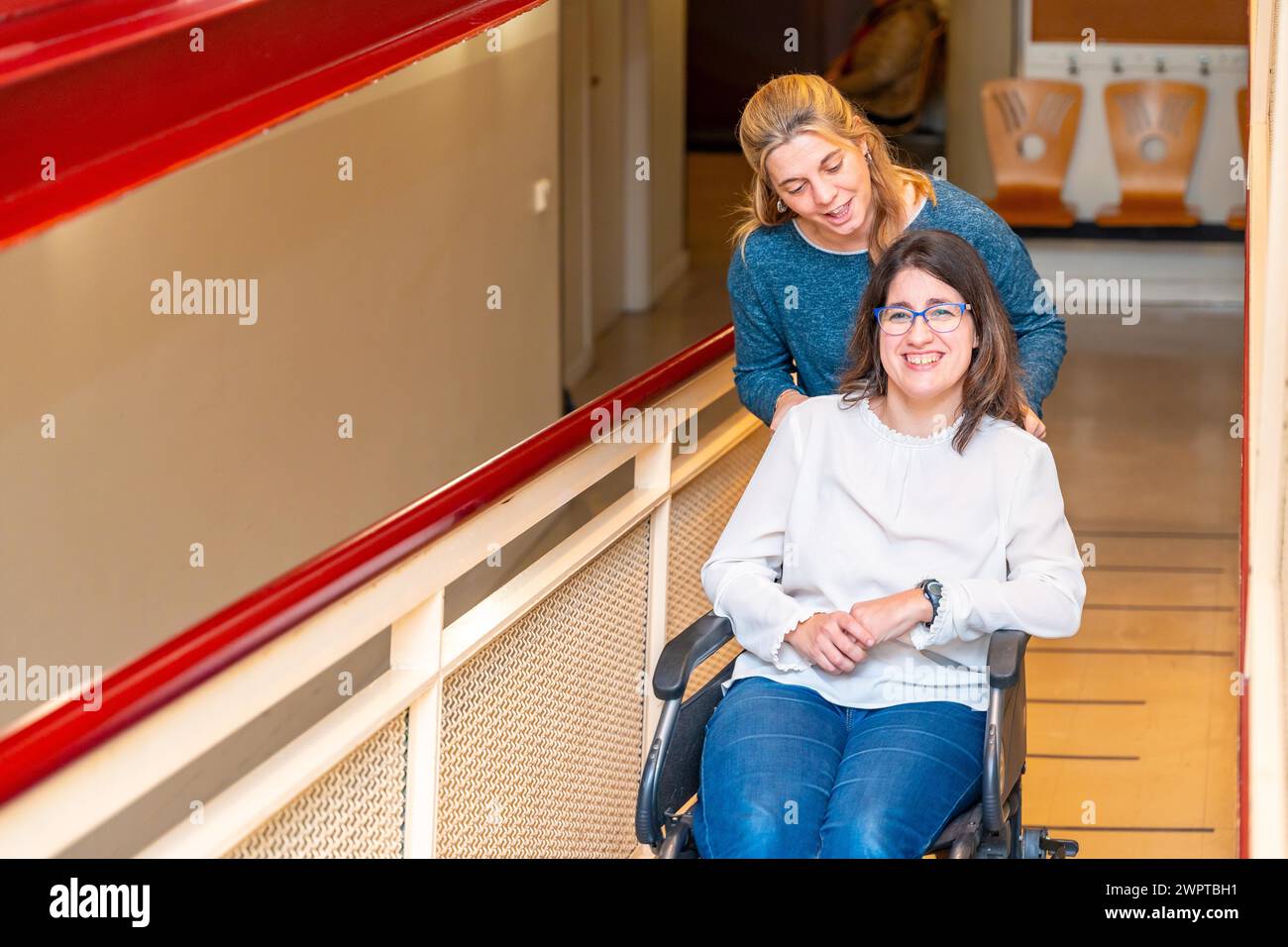 Donna che cammina una donna disabile mentale in sedia a rotelle lungo un centro di assistenza diurna Foto Stock