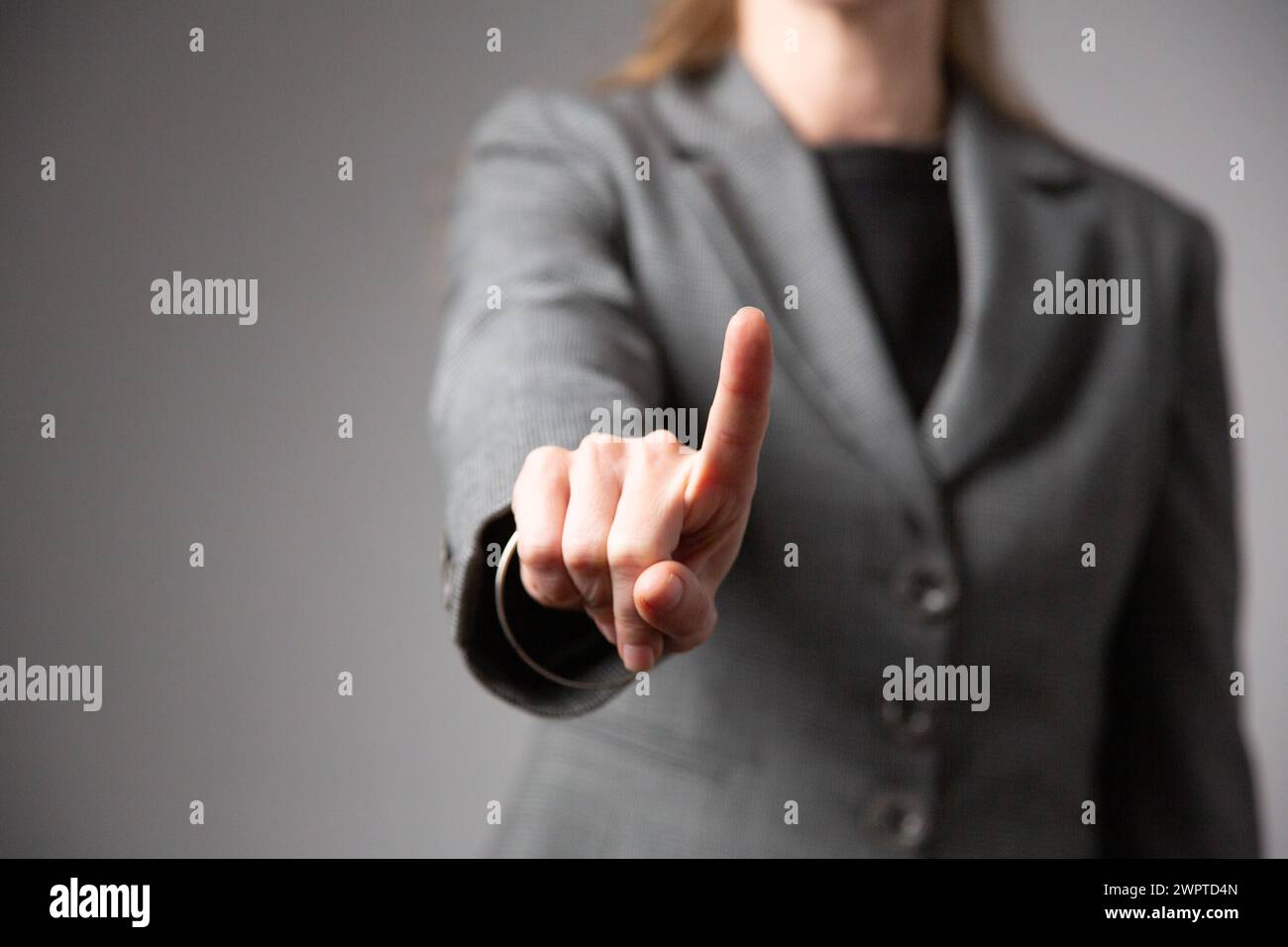 Primo piano di una donna d'affari con il braccio allungato in avanti e il dito indice senza volto. Sfondo grigio. Foto Stock