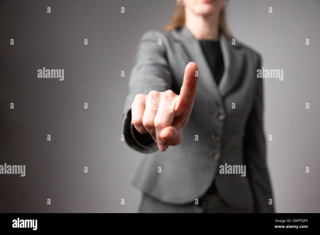 Ritratto di una donna d'affari con il braccio esteso in avanti e il dito indice senza volto. Sfondo grigio. Foto Stock