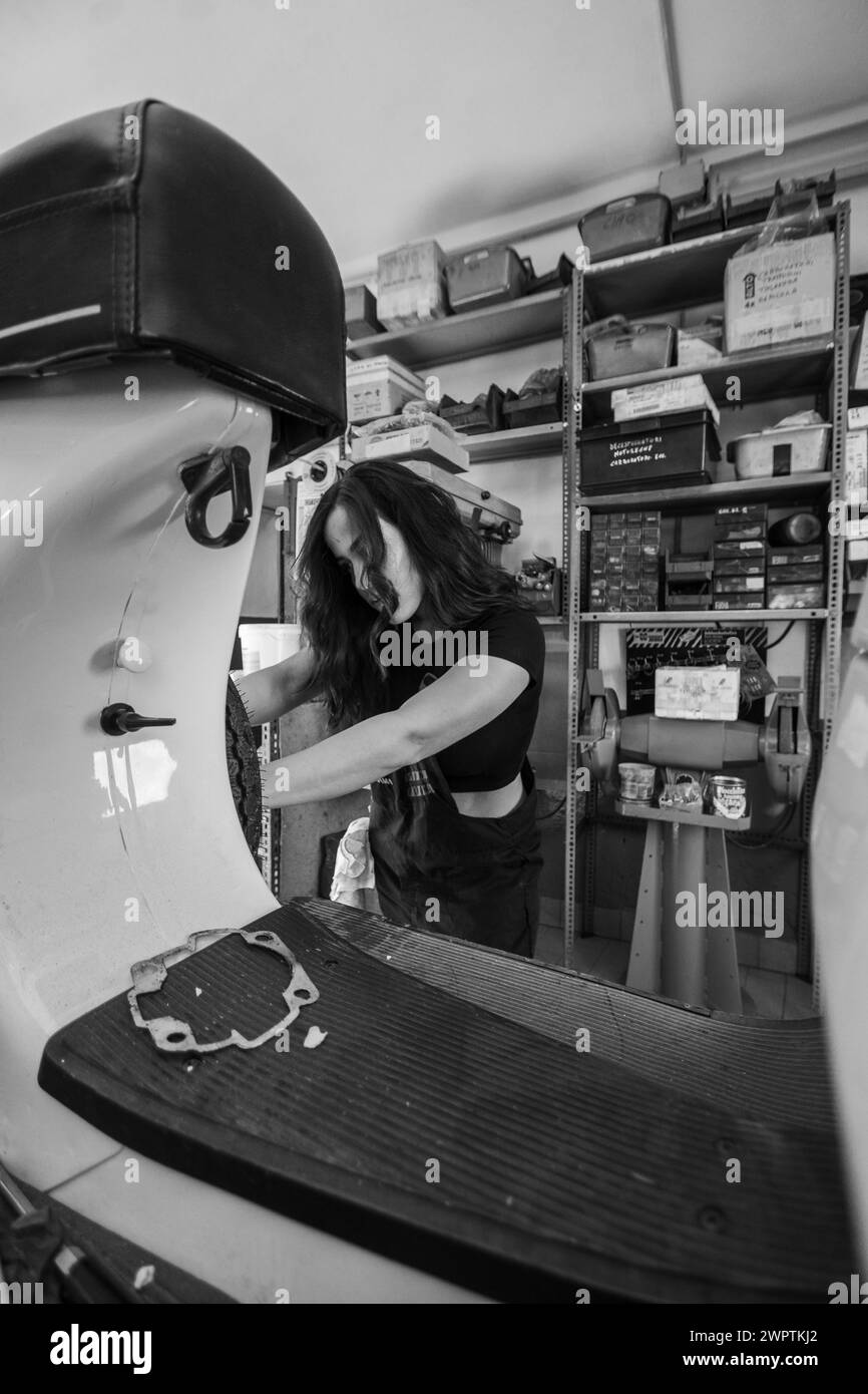 Meccanico donna che si occupa di riparare l'interno di uno scooter italiano d'epoca in un'officina, donne vere che svolgono lavori tradizionali da uomo della Foto Stock
