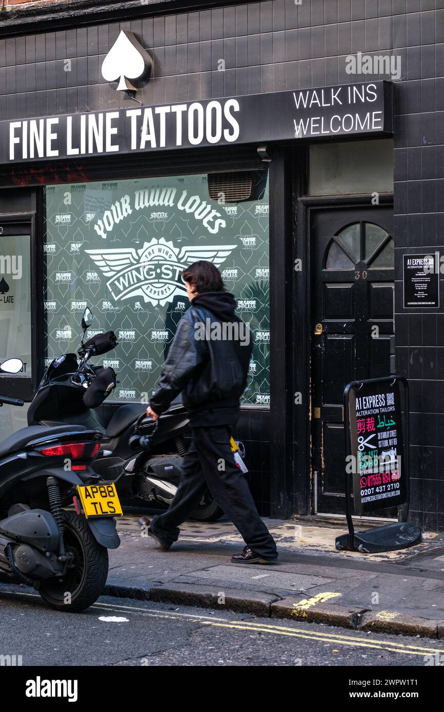 Soho, Londra, Regno Unito, 8 marzo 2024, Man Walking Past fine Line Tattoo Shop con Motor Scooter parcheggiato all'esterno Foto Stock