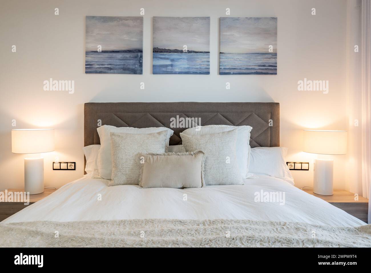 un'immagine ravvicinata di un letto ricoperto di cuscini con lampade da comodino e opere d'arte appese sopra la testa Foto Stock