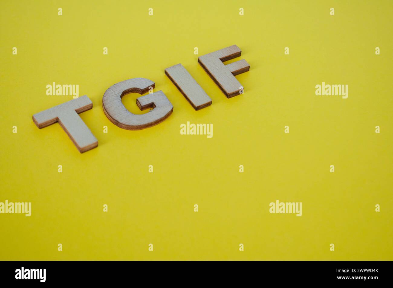 Le lettere di legno TGIF che rappresentano Grazie a Dio sono venerdì su sfondo giallo. Foto Stock