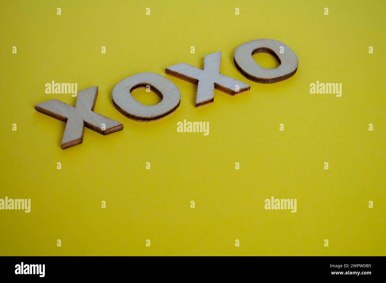 XOXO lettere in legno che rappresentano abbracci e baci su sfondo giallo. Foto Stock