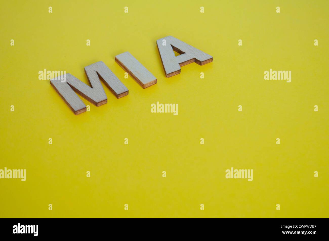 Lettere in legno MIA che rappresentano Missing in Action su sfondo giallo. Foto Stock