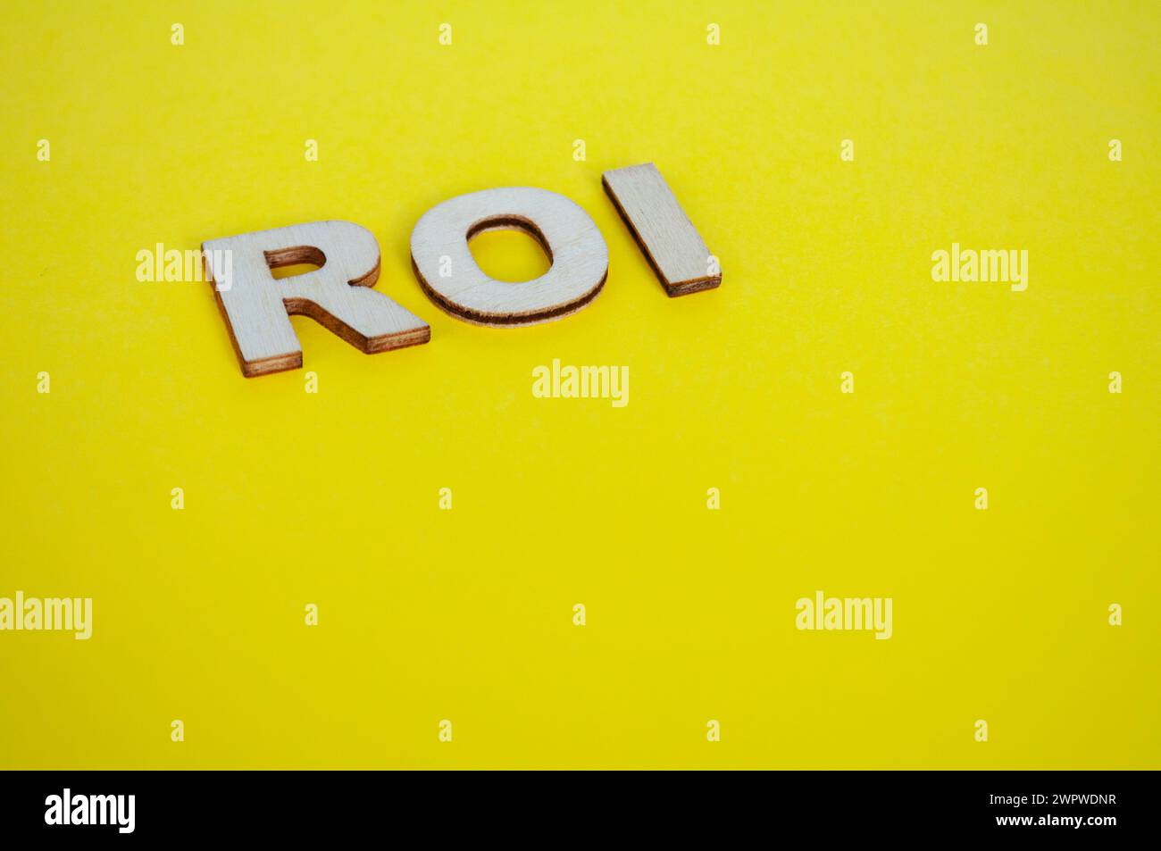 ROI lettere in legno che rappresentano il ritorno sull'investimento su sfondo giallo. Foto Stock
