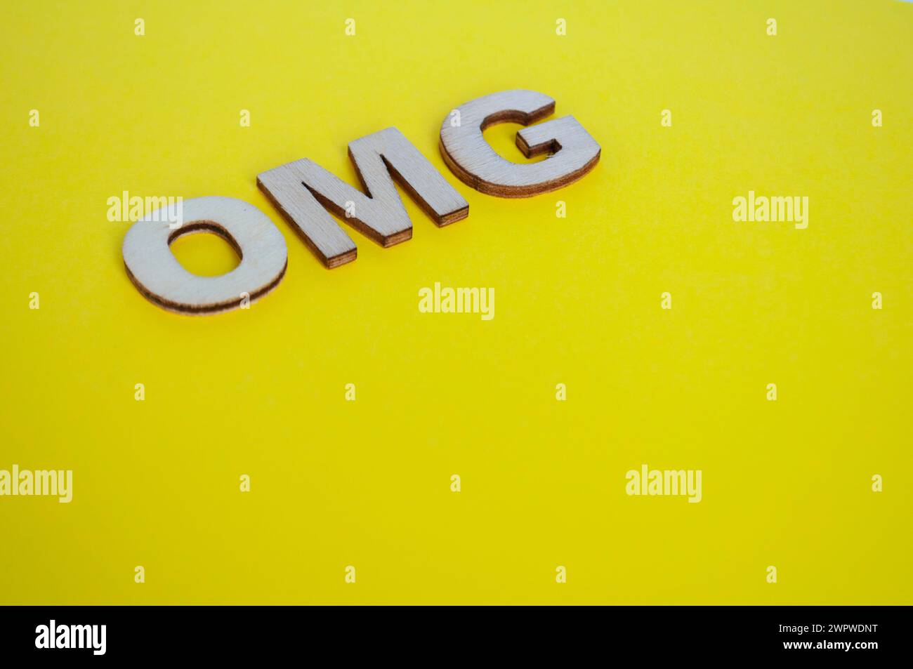 Lettere di legno OMG che rappresentano Oh mio Dio su sfondo giallo. Foto Stock