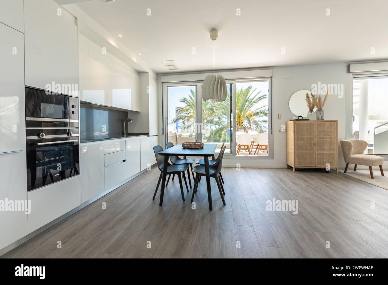una cucina a vista con tavolo da pranzo nero che porta alla terrazza con balcone aperto negli appartamenti mediterranei Foto Stock