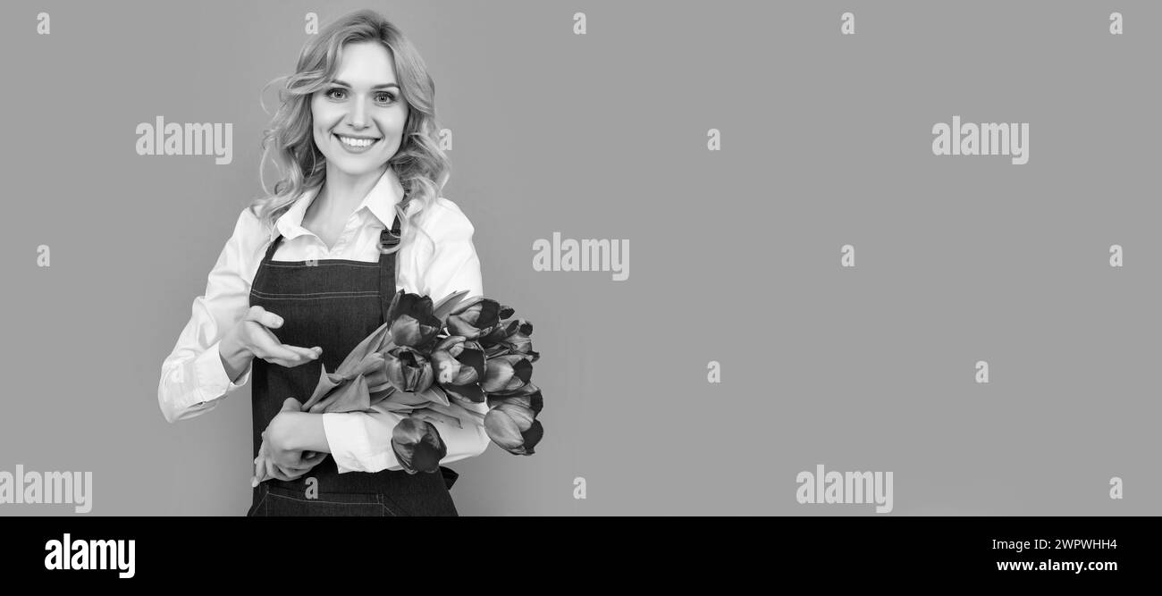 ragazza sorridente in grembiule con fiori di tulipano primaverile su sfondo grigio. Donna isolato volto ritratto, banner con mock up spazio copia. Foto Stock