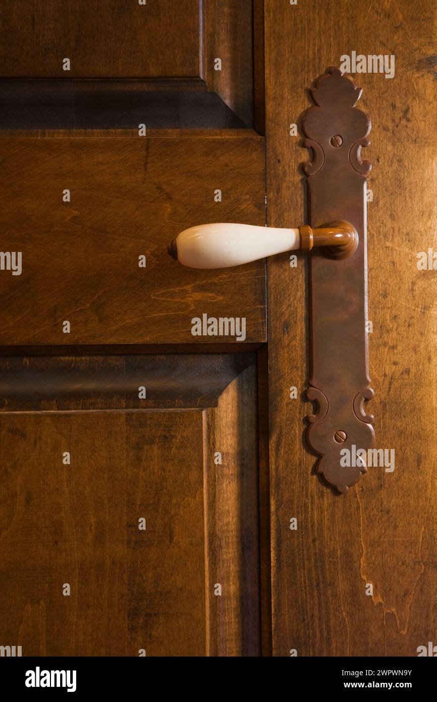 Antica maniglia per porta in porcellana bianca su una vecchia porta in legno nella camera da letto principale al piano superiore all'interno della casa in legno. Foto Stock