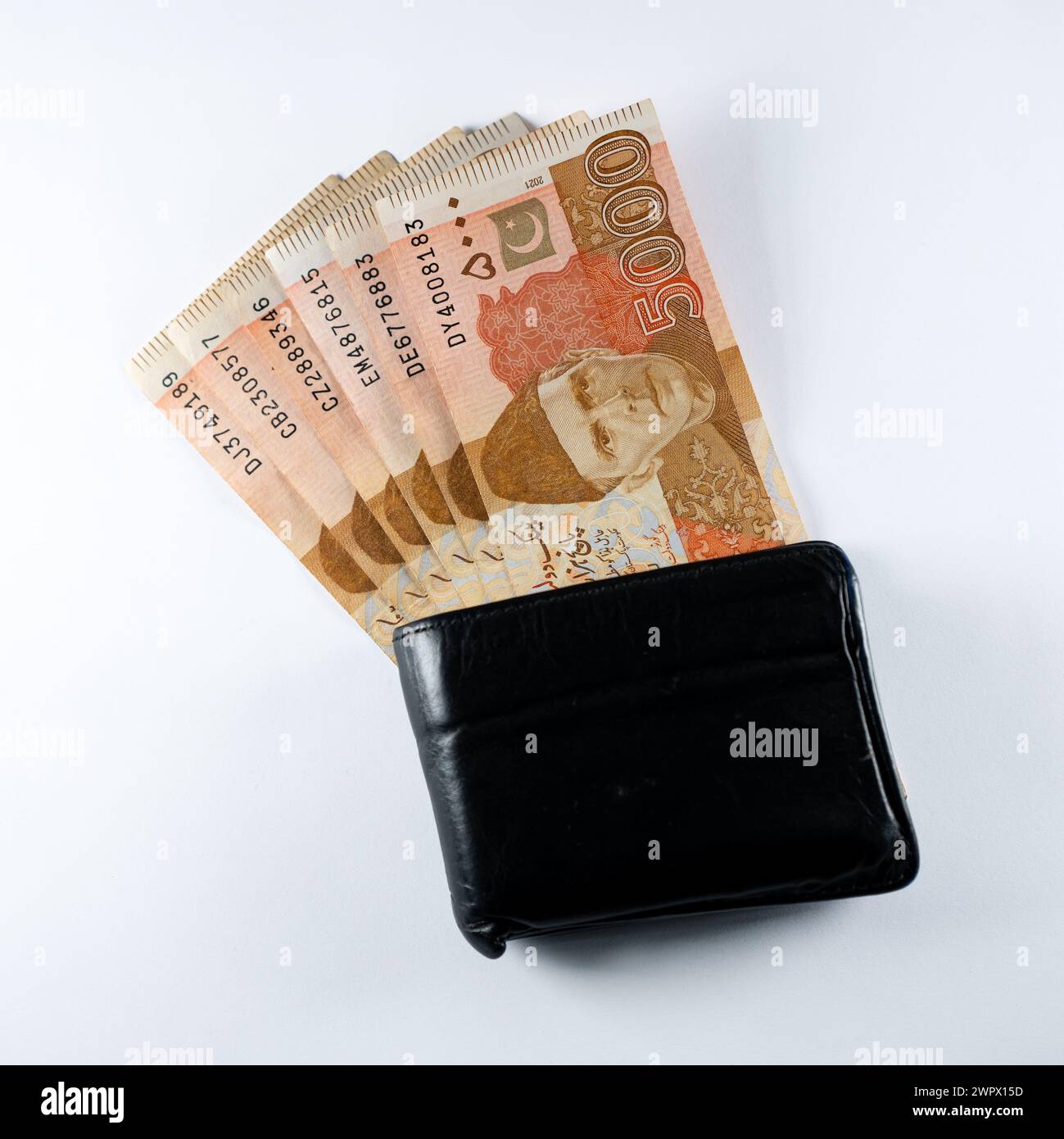 Cinquemila banconote da 5000 rupie allineate a un portafoglio nero in pelle. Banconote ufficiali della Banca statale pakistana 2024 isolate sul backgroud bianco. Foto Stock