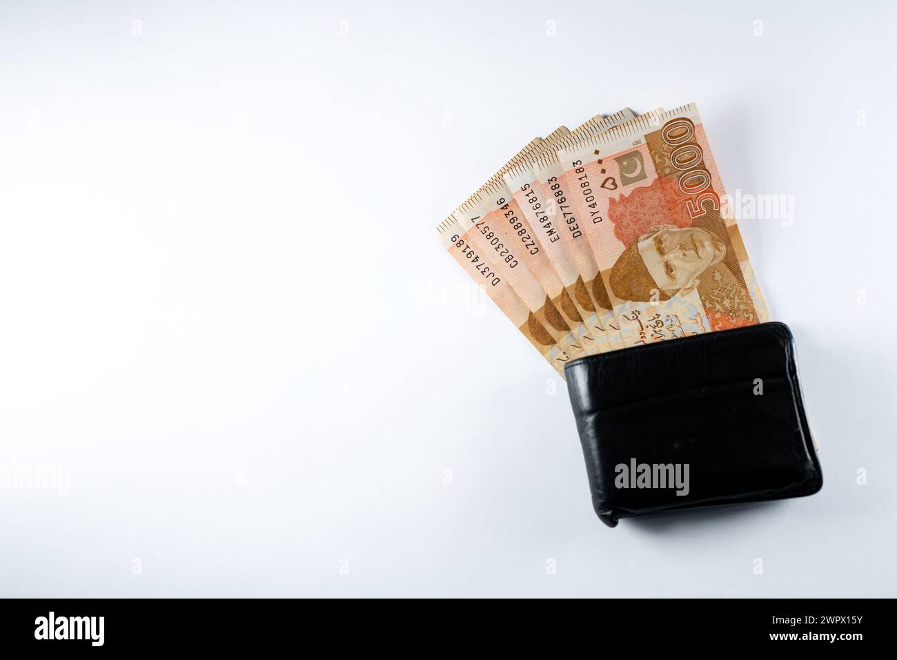 Cinquemila banconote da 5000 rupie allineate a un portafoglio nero in pelle. Banconote ufficiali della Banca statale pakistana 2024 isolate sul backgroud bianco. Foto Stock