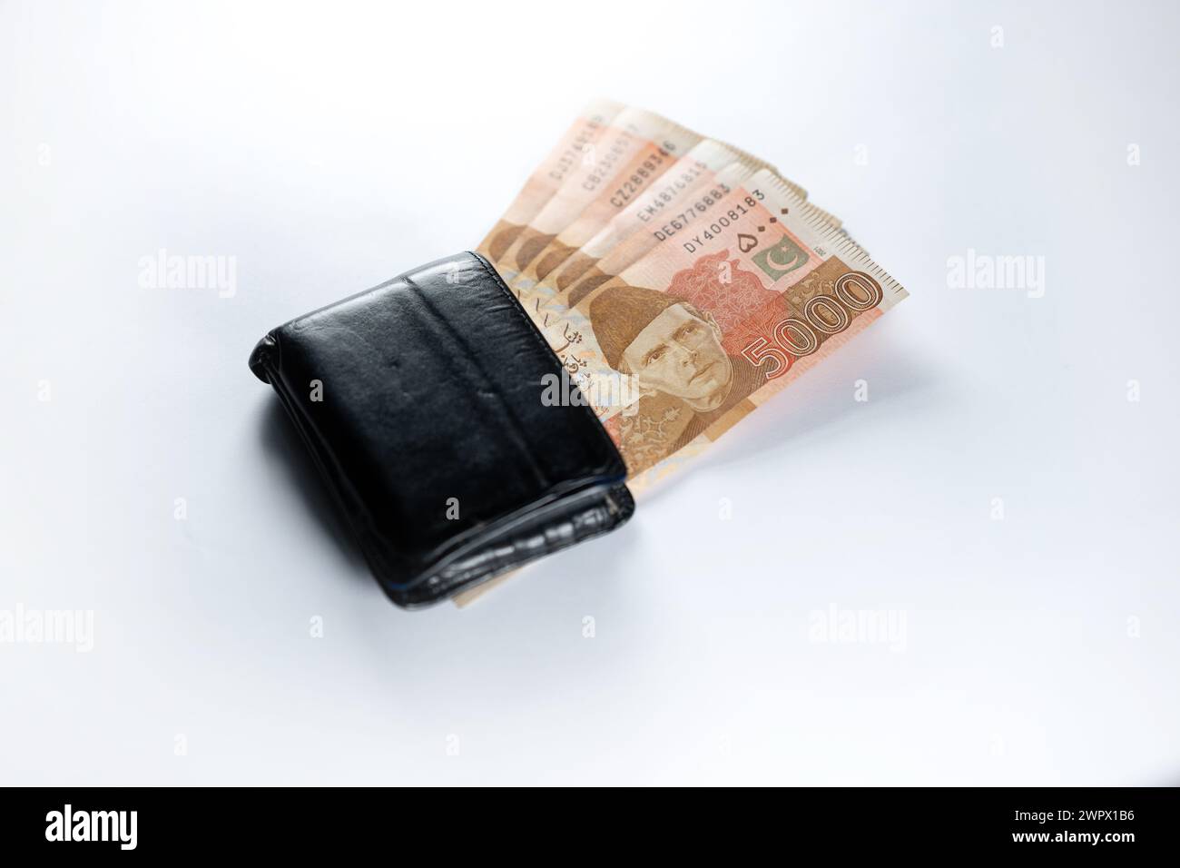 Cinquemila banconote da 5000 rupie allineate a un portafoglio nero in pelle. Banconote ufficiali della Banca statale pakistana 2024 isolate sul backgroud bianco. Foto Stock