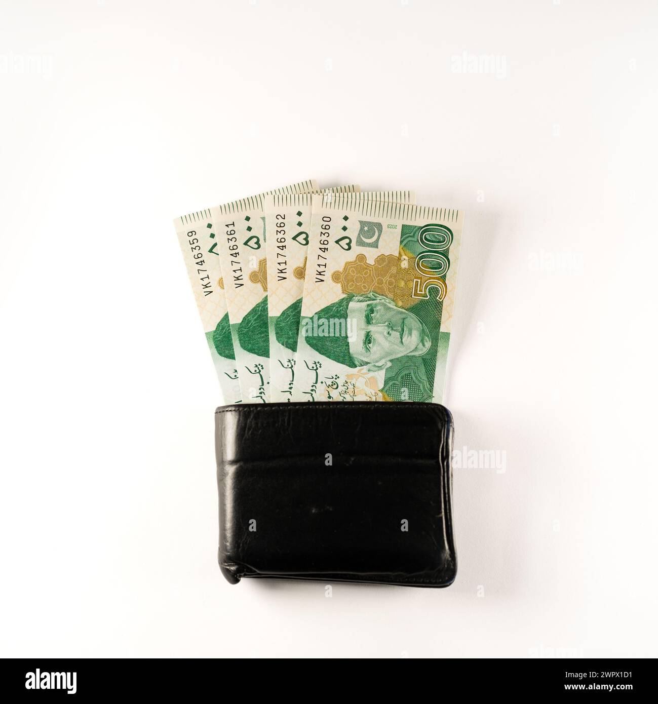 Cinquecento banconote in rupie allineate a un portafoglio nero in pelle. Banconote ufficiali della Banca statale pakistana 2024 isolate su sfondo bianco. Foto Stock