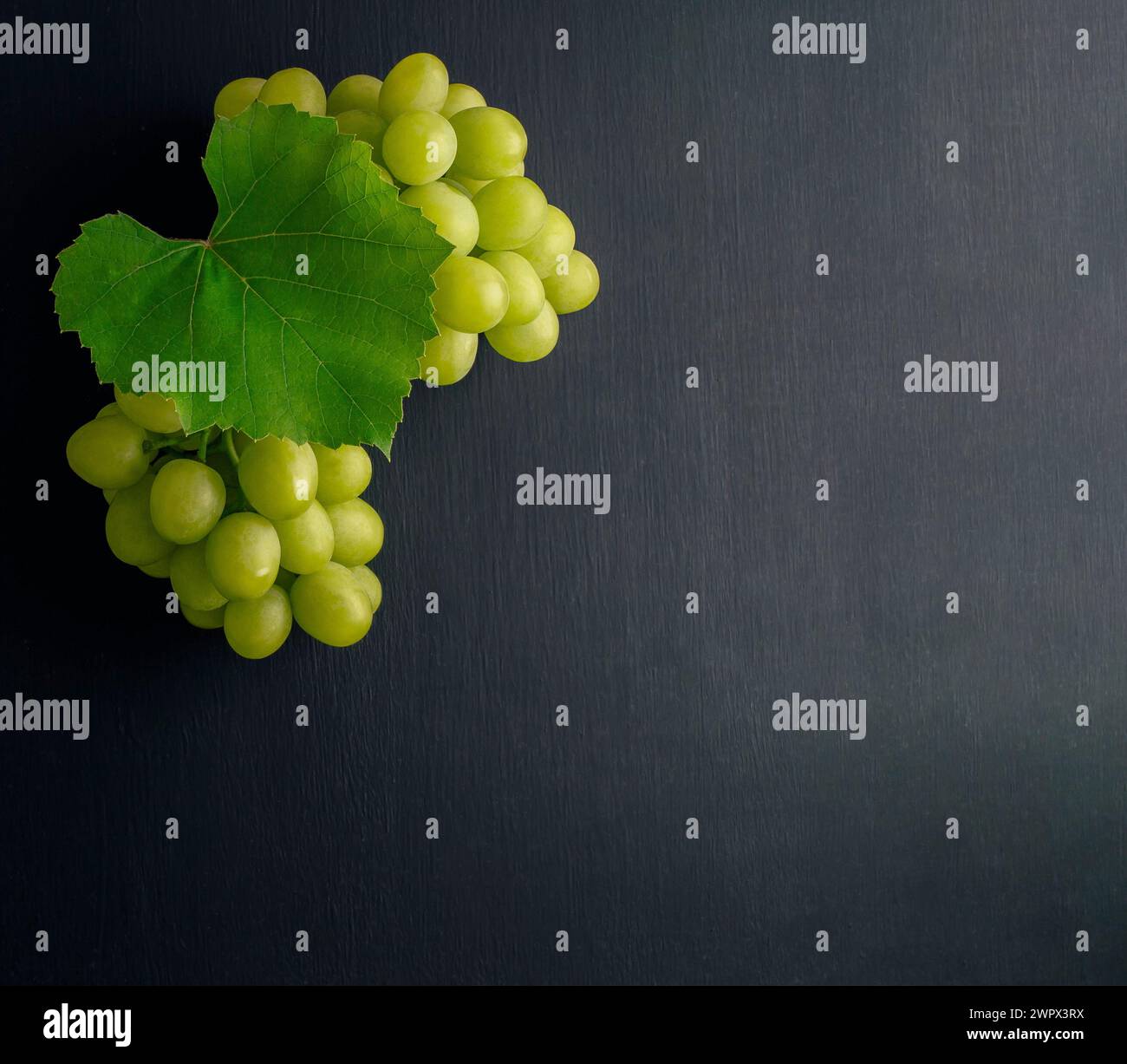 Un mucchio d'uva. Concetto di agricoltura e vinificazione. grappoli di uva con foglie su sfondo rustico scuro. La composizione del vino è piatta su un tavolo nero. Foto Stock