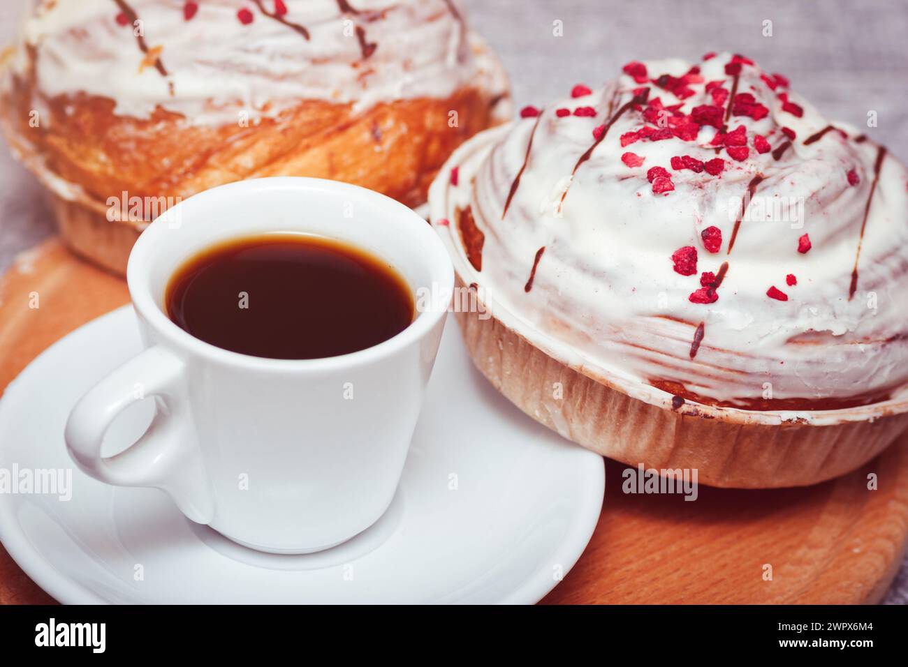Tazza di caffè espresso con biscotti dolci Cinnabon. Pasta gustosa con glassa di panna e decorazione rosa. Foto Stock