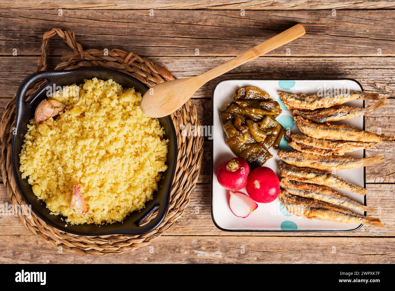 Piatto di migas con il suo accompagnamento, peperoni arrostiti, acciughe fritte e ravanelli, su un tavolo rustico. Foto Stock