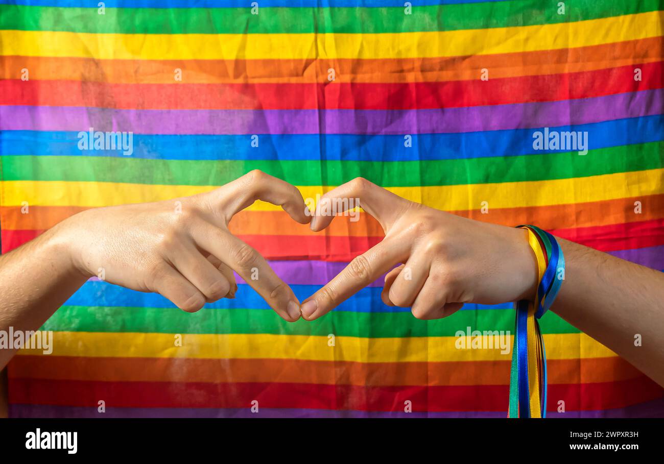 Due mani si uniscono per formare un cuore con sfondo della bandiera LGBT. Concetto di giorno dell'orgoglio gay e amore tra razze diverse, esseri umani contro discriminati Foto Stock