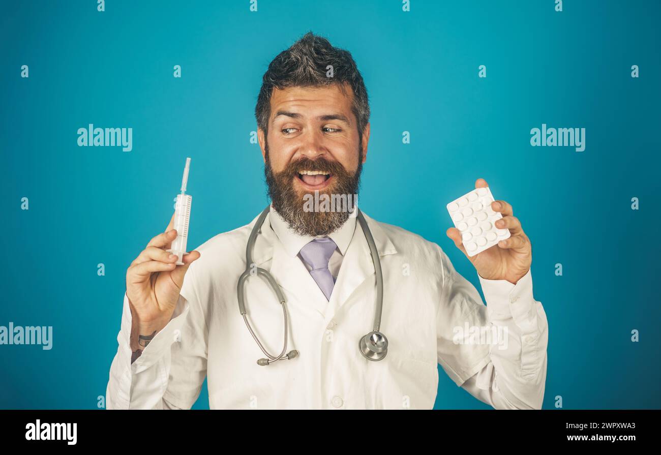 Medico professionista sorridente con siringa e pillole in blister. Medico barbuto in abito medico bianco con stetoscopio. Concetto di Foto Stock