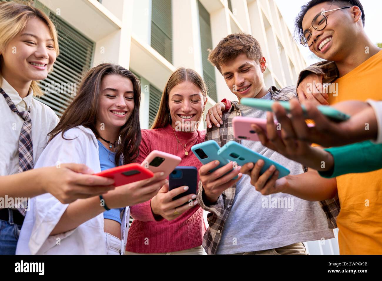 Gruppo di generazioni multirazziali z giovani sorridono volentieri guardando video divertenti su uno smartphone Foto Stock