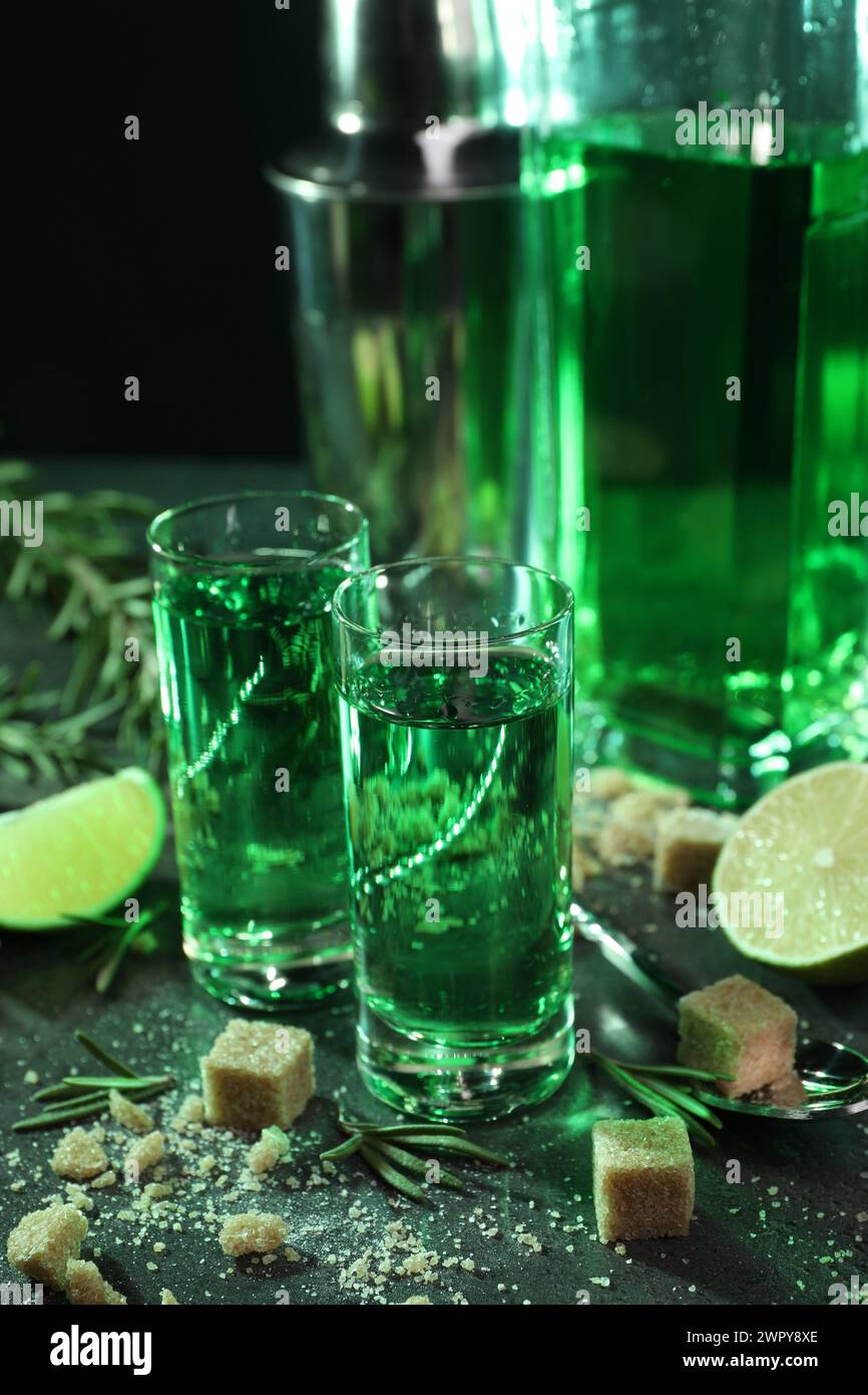 Absinthe in bicchieri da shot, cucchiaio, zucchero di canna, lime e rosmarino su un tavolo grigio, primo piano. Bevanda alcolica Foto Stock