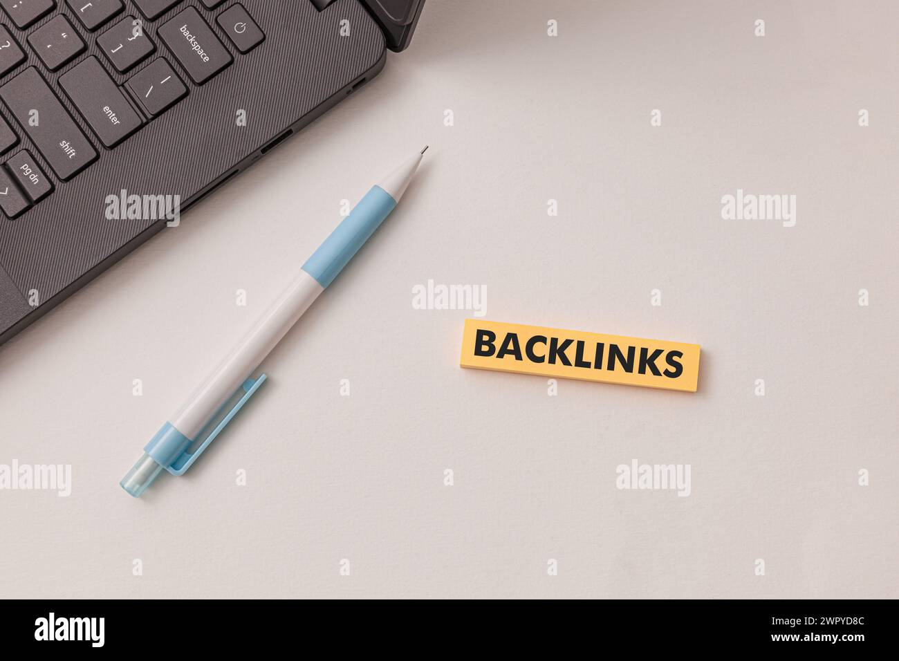 Laptop nero, penna blu, adesivo giallo con testo Backlinks sulla scrivania bianca. Concetto migliorare la visibilità del sito Web e le classifiche sui motori di ricerca Foto Stock