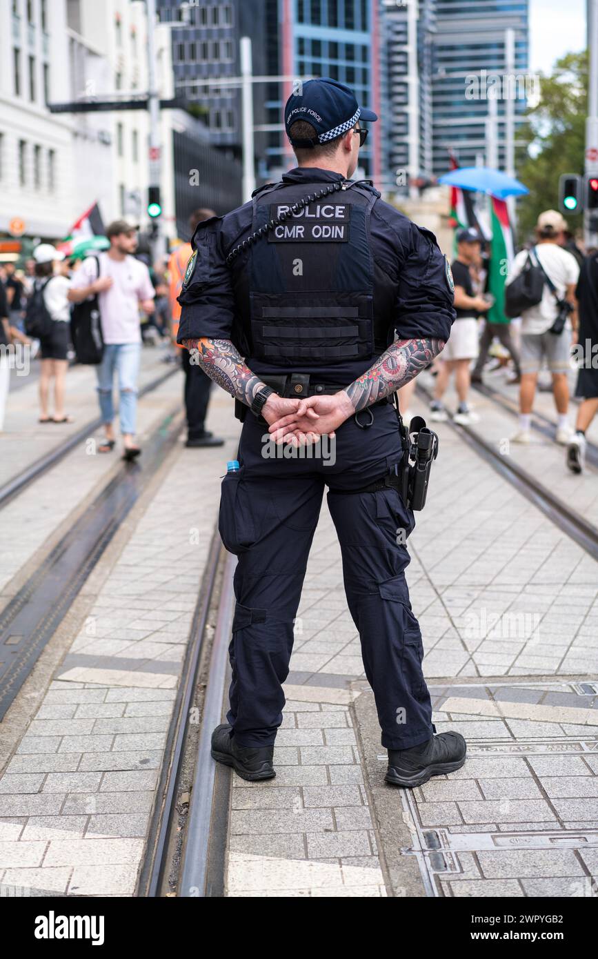Un poliziotto con tatuaggi monitora i manifestanti durante una marcia di Sydney a sostegno dei palestinesi nella guerra di Gaza. Foto Stock