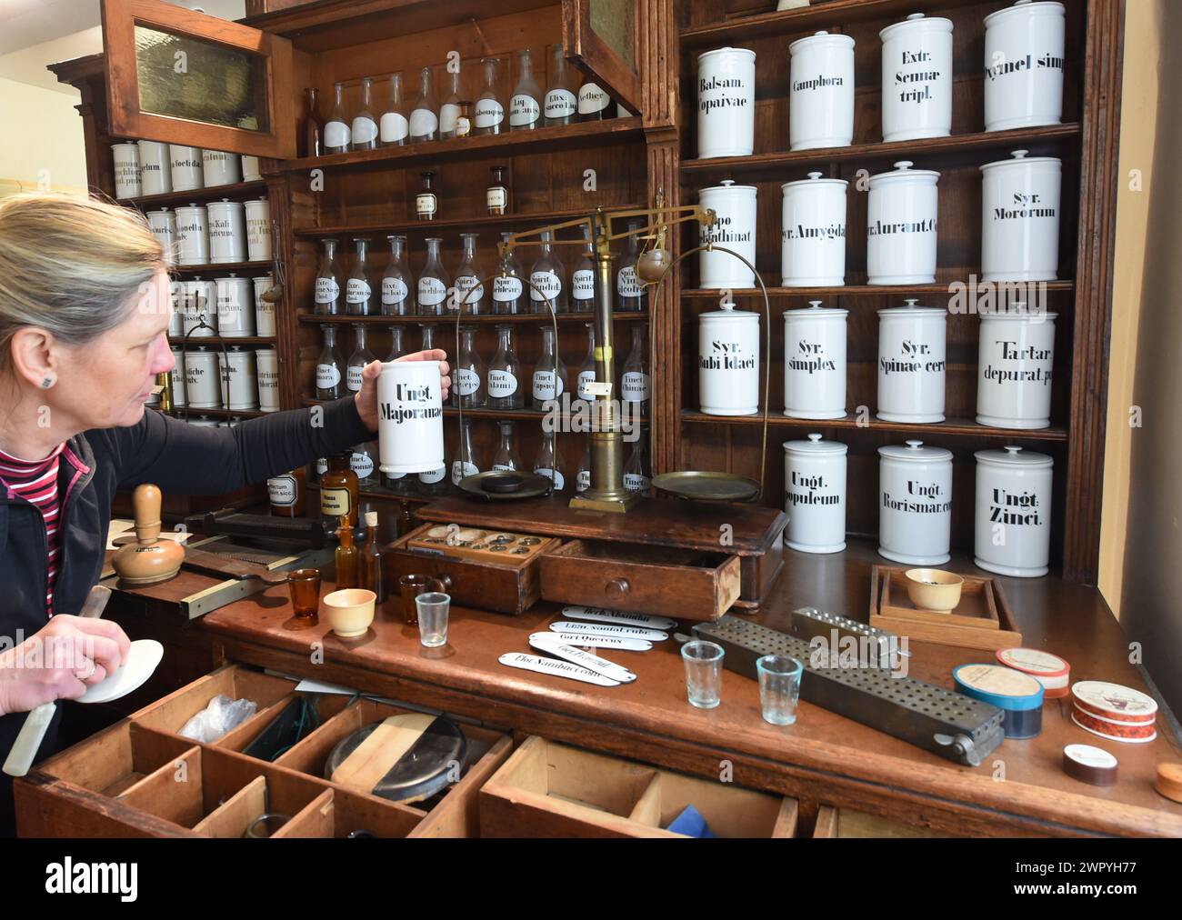 29 febbraio 2024, Sassonia-Anhalt, Naumburg: Nel museo della storica farmacia Löwen-Apotheke, il farmacista Kerstin Reh organizza gli utensili presso una postazione di prescrizione dal 1897. La farmacia, gestita dalla famiglia del direttore della farmacia Dr. Andreas Hünerbein da 120 anni, è una delle poche istituzioni del suo genere in Germania che si trova nello stesso luogo da oltre 400 anni e da cui molti oggetti possono essere esposti in un museo. Le mostre del museo includono il privilegio di farmacia del 1635 emesso dall'elettore di Sassonia, Johann Georg i, strumenti per la produzione di estratto Foto Stock