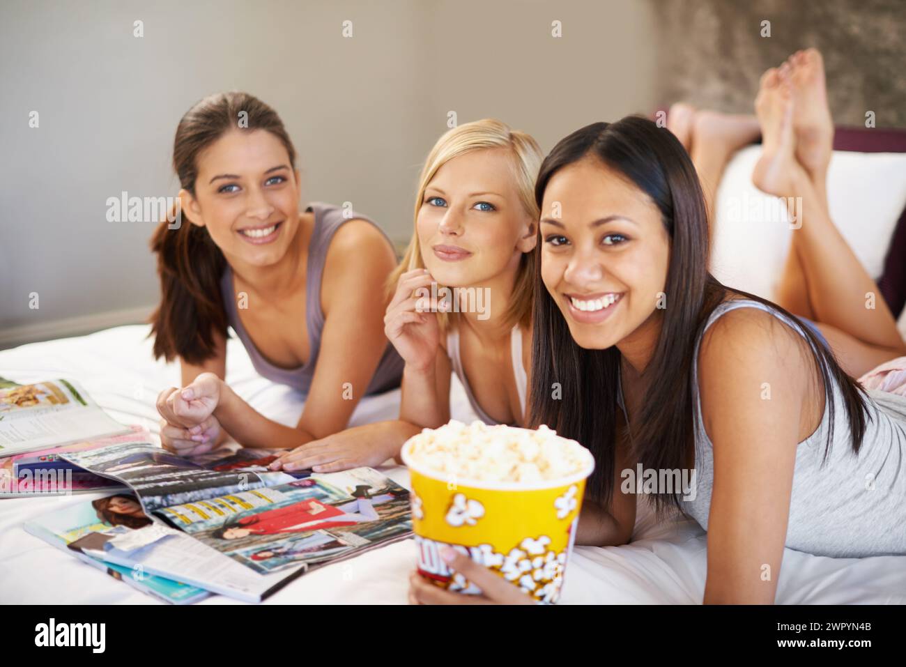 Amici, popcorn e ritratti per dormire, socievoli e camere da letto per legare e gruppi entusiasti per spuntini. Donne, insieme e riviste per Foto Stock