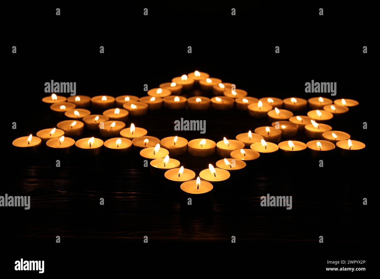 Stella di Davide fatta con candele brucianti su sfondo nero. Giorno della memoria Foto Stock