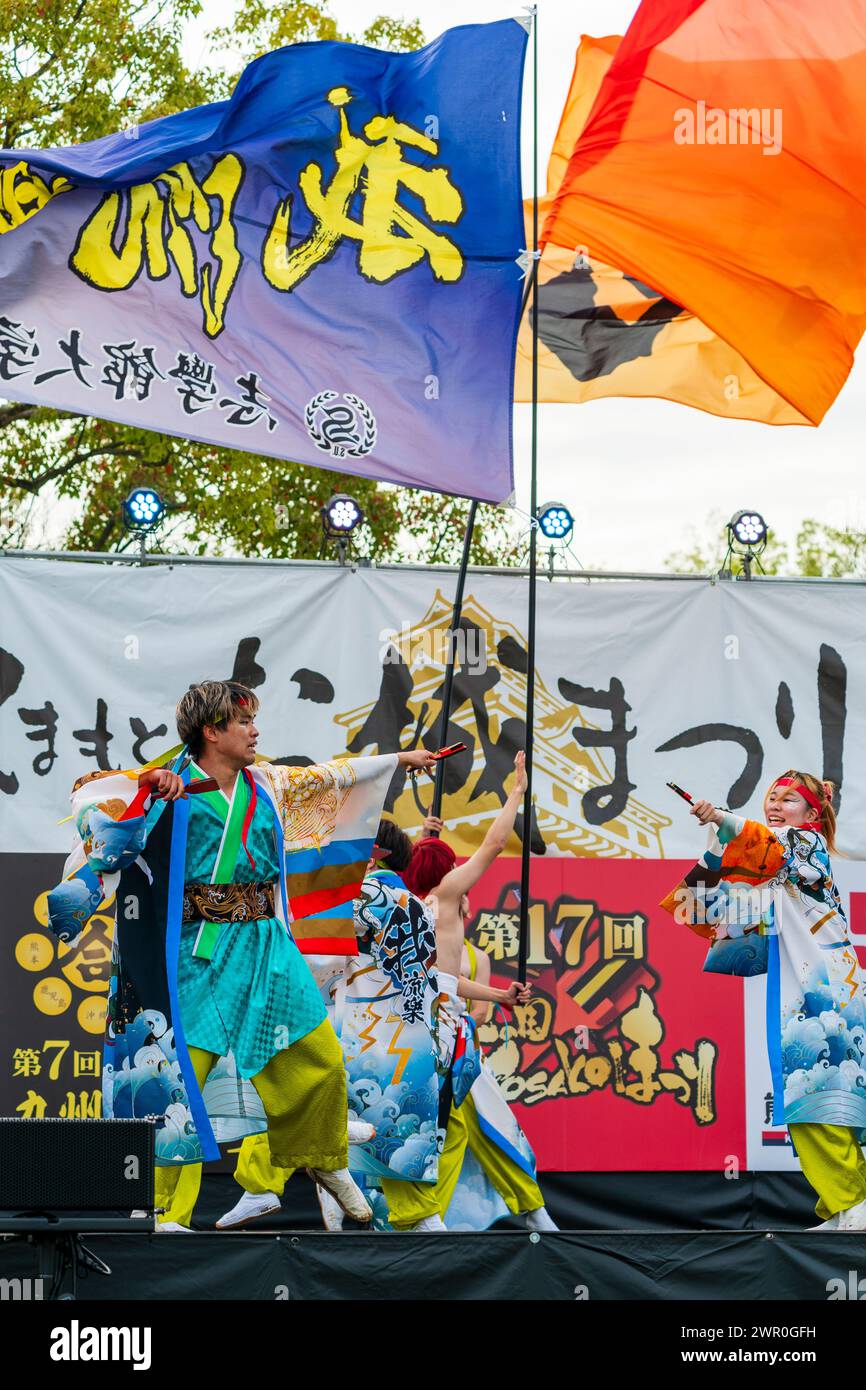 Ballerini giapponesi Yosakoi che tengono naruko sul palco con due striscioni che volano dietro di loro al festival di danza Kumamoto Kyusyu Gassai. Foto Stock