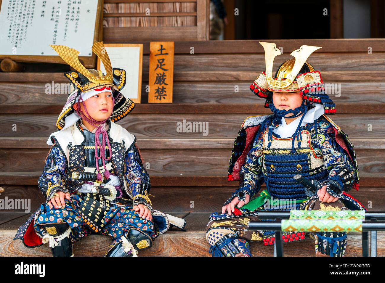 Due giovani bambini giapponesi vestiti con un'armatura completa di samurai, seduti su gradini di legno del luogo Honmaru al castello di Tatsuno durante la parata dei samurai. Foto Stock