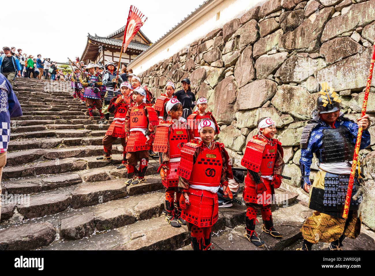 Giovani ragazze giapponesi vestite di armatura rossa come soldati ashigaru in attesa sui gradini del castello di pietra a Tatsuno durante la parata dei samurai in primavera Foto Stock