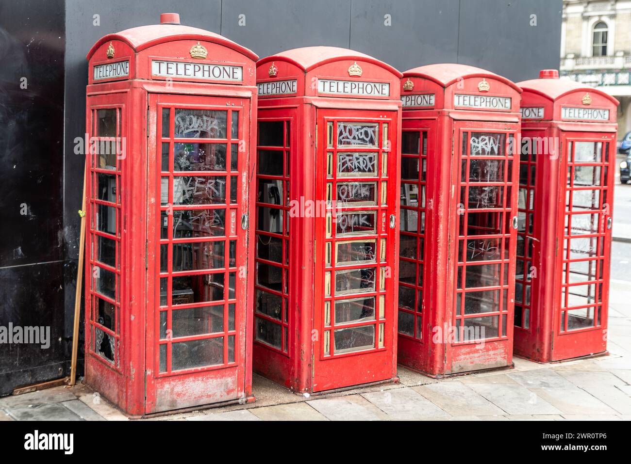 Fila di iconiche cabine telefoniche rosse vandalizzate a Londra, Regno Unito. Quattro telefoni vintage con finestre rotte e graffiti Foto Stock
