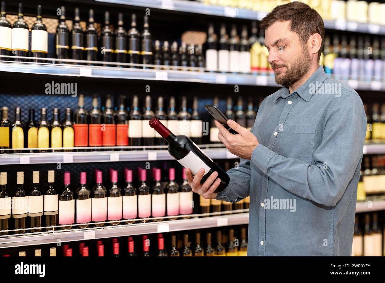 Uomo cliente che legge e-label su una bottiglia di vino utilizzando il suo smartphone. Foto Stock