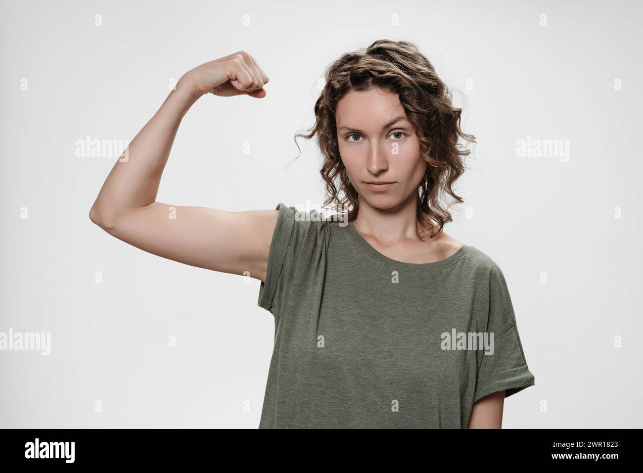 La giovane donna dai capelli ricci mostra muscoli sulla mano, si sente orgogliosa di essere forte e avere forza, mostra il suo grande potere Foto Stock